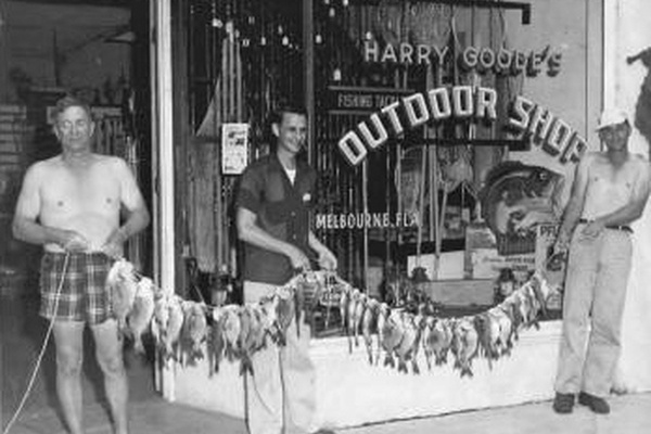 Black and white photo of the front of Harry Goode's outdoor shop with three men holding fish
